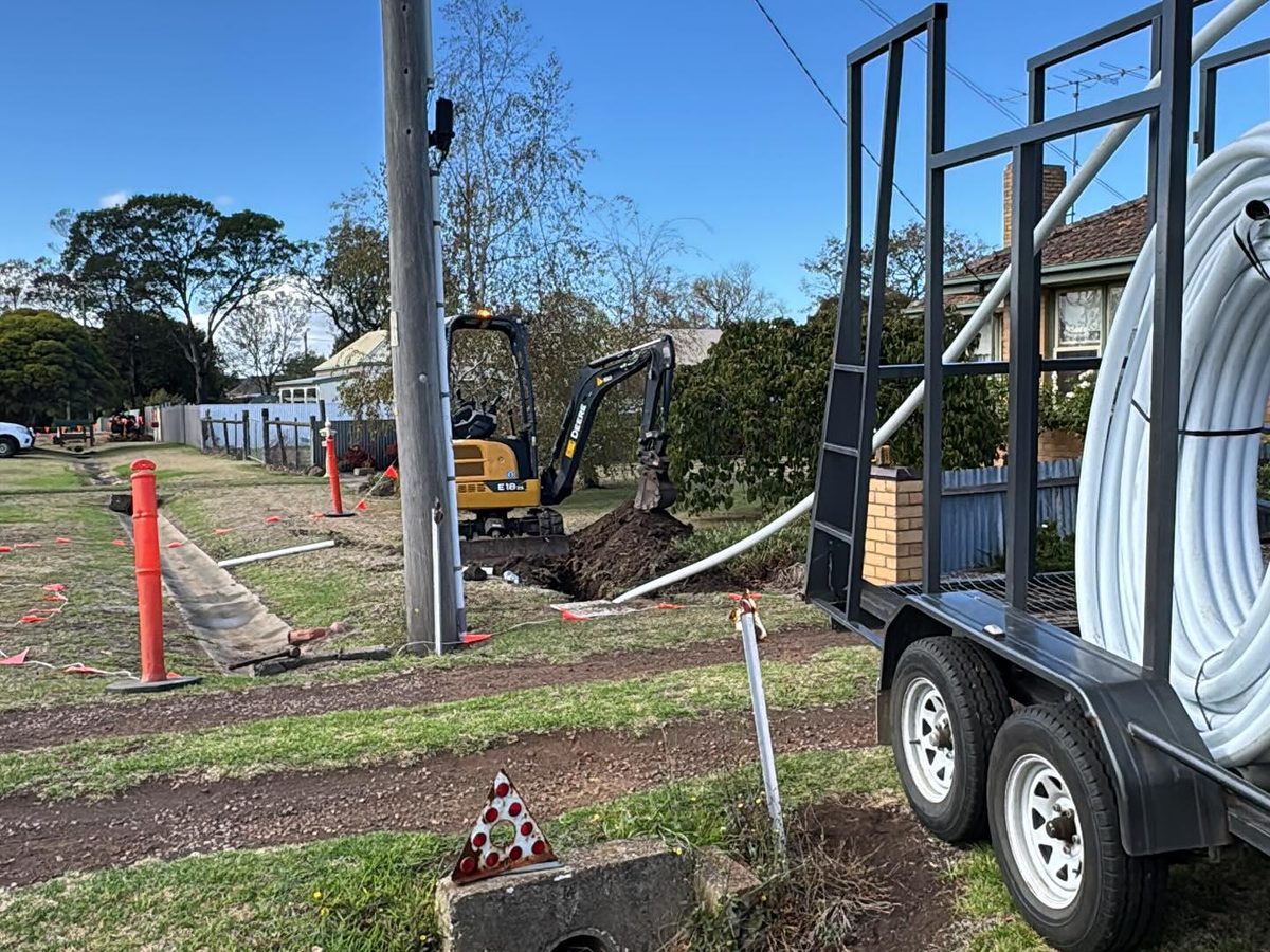 A trailer loaded with a coil of white HDPE conduit beside a mini excavator on a residential job