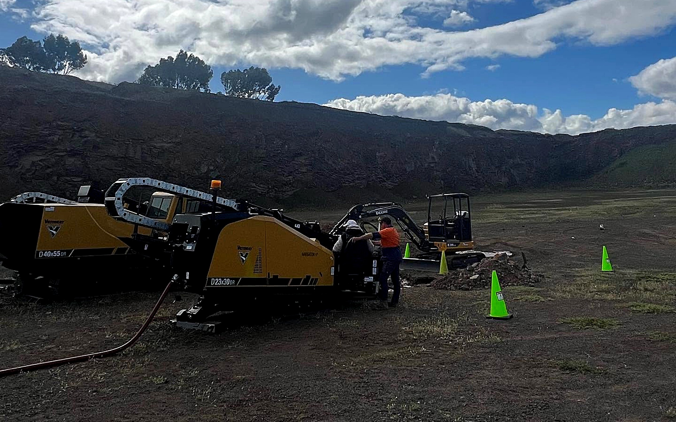 Two All Network Connections Vermeer directional drilling rigs set up on an open site with the crew at the controls and an excavator working the entry pit